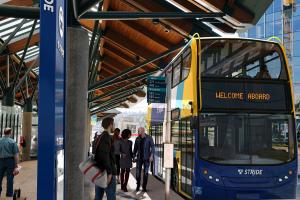 A rendering of people waiting at a bus stop for an approaching double decker Stride bus