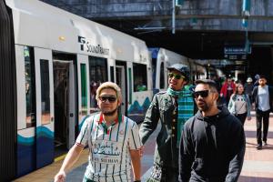 Three people in soccer jerseys walk along the sunny platform at International District Chinatown Station.