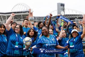 A group of about 10 people wear soccer jerseys and cheer
