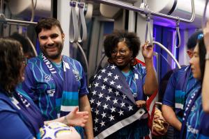 Four people wearing blue jerseys ride a Link train