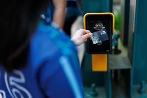 A passenger wearing a blue jersey taps an ORCA card on a yellow reader