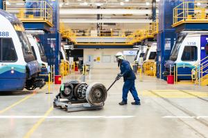 A worker wearing blue pushes a cart with train parts through the brightly lit Operations and Maintenance Facility for Link light rail vehicles