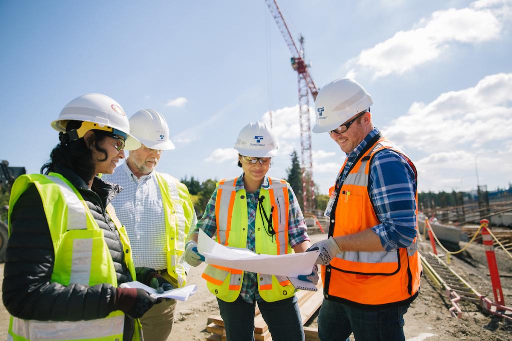 Four Sound Transit employees in bright vests and hard hats review construction plans.