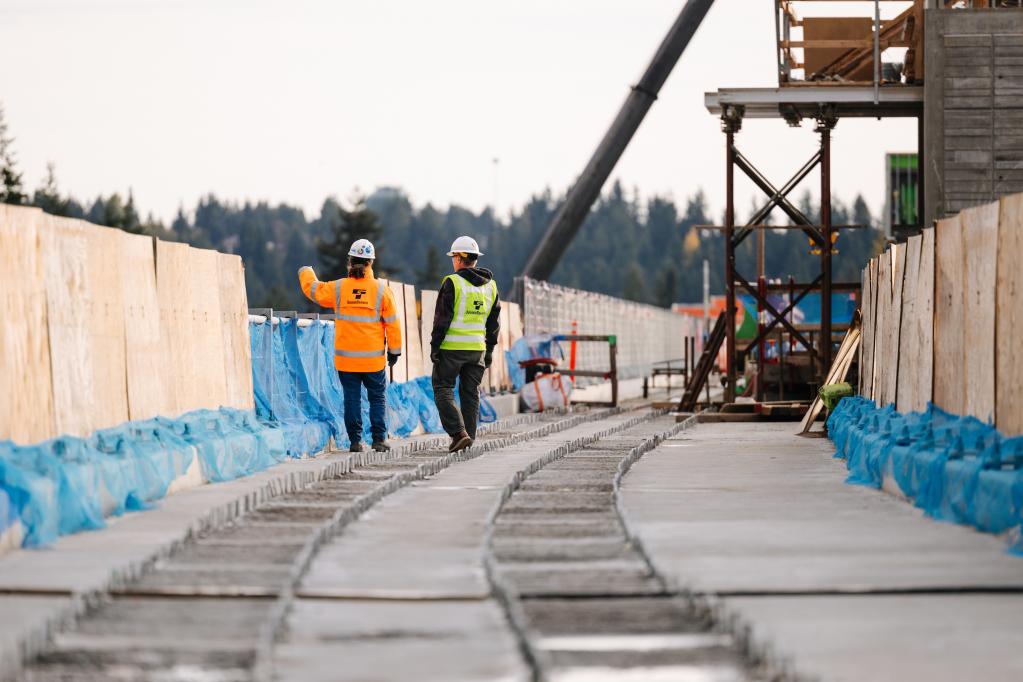 Two people walk on a light rail guideway under construction.