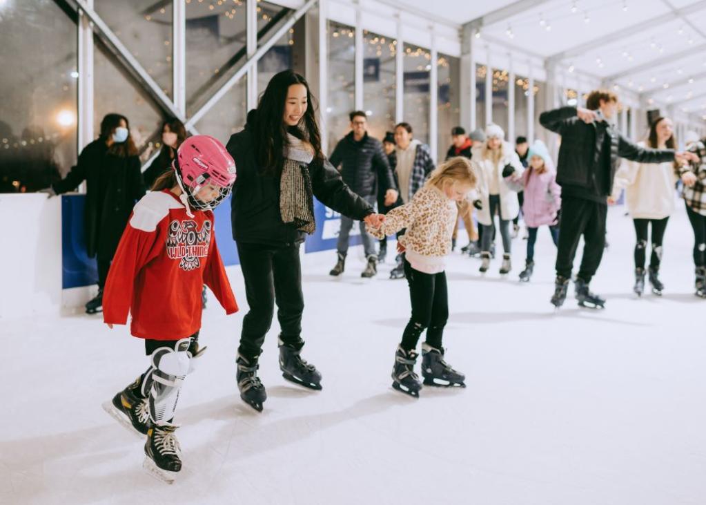 Three people hold hands while ice skating at an outdoor rink in Bellevue