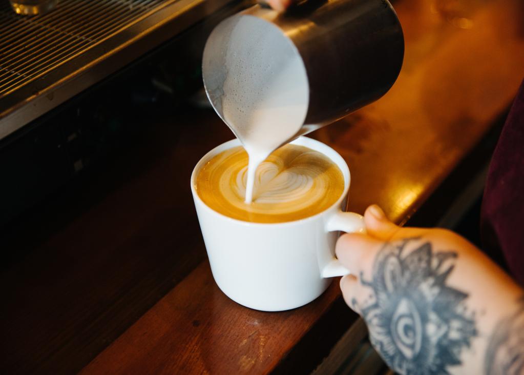 A barista pours milk into a latte
