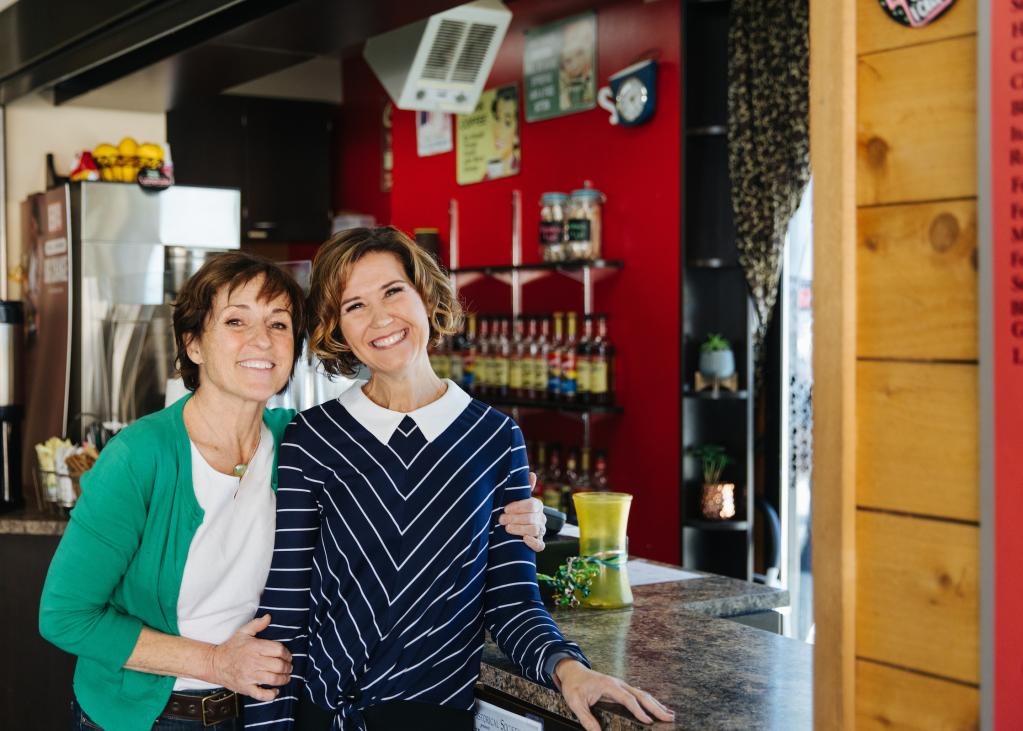 Two women hug with one hand and hold a cup of coffee in the other 