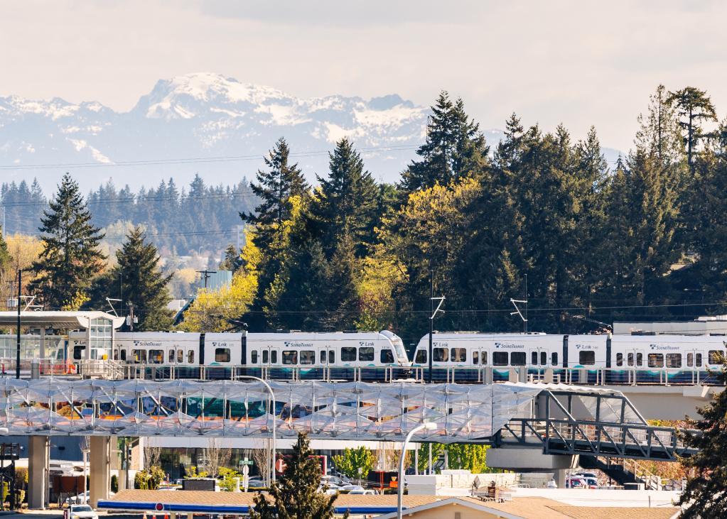 A 2 Line train at Wilburton Station, with trees and mountains in the background and the nearby pedestrian bridge in the front