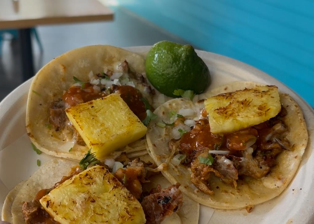 Three tacos on a plate with pineapple on top, and a lime on the side.