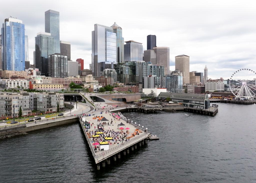 A drone shot of Pier 62 with the Seattle skyline, including the Great Wheel, in the background.