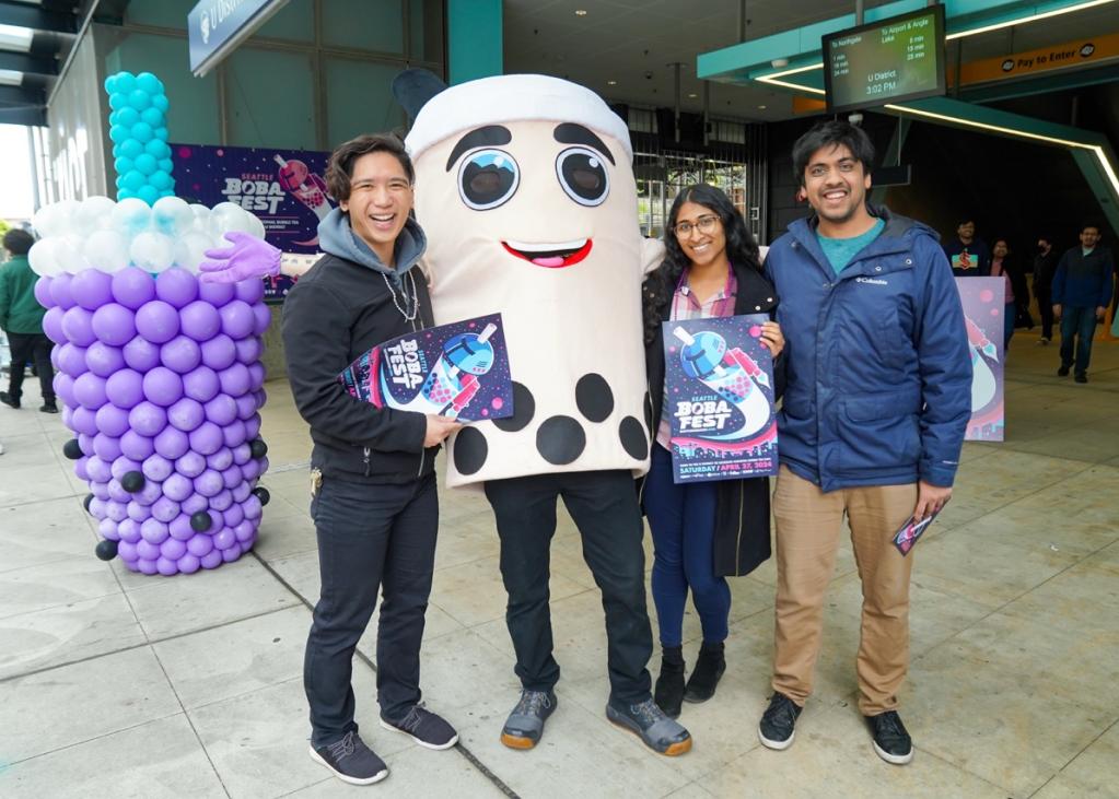 Three people pose with a mascot that looks like bubble tea