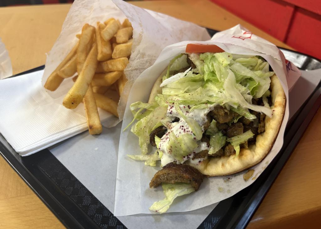 A gyro with lettuce and tomato and sauce on a red tray next to fries in a paper bag