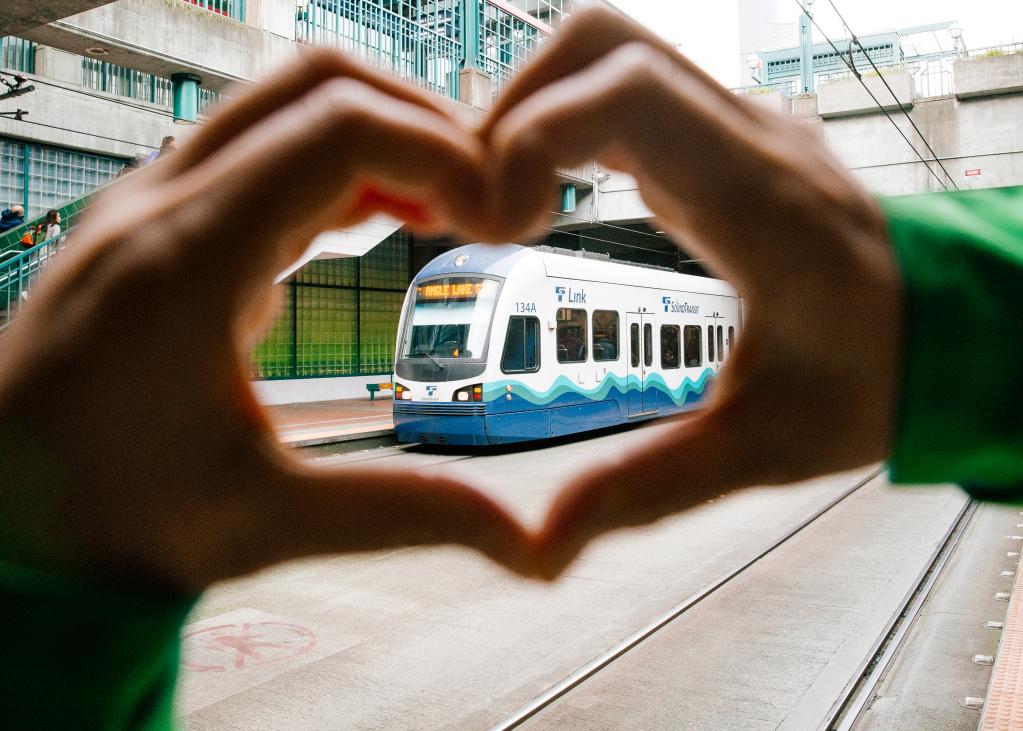 A person makes 'heart hands' around a Link train at International District/Chinatown Station,