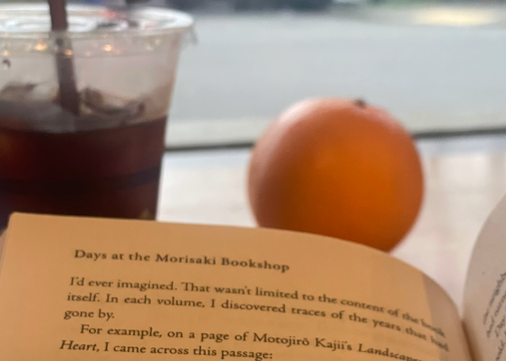 A book, an iced coffee, and an orange on a table