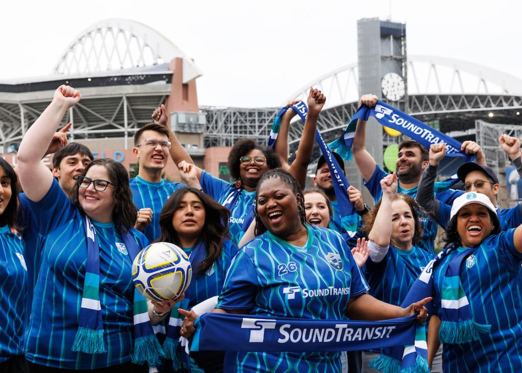 A group of about 10 people wear soccer jerseys and cheer