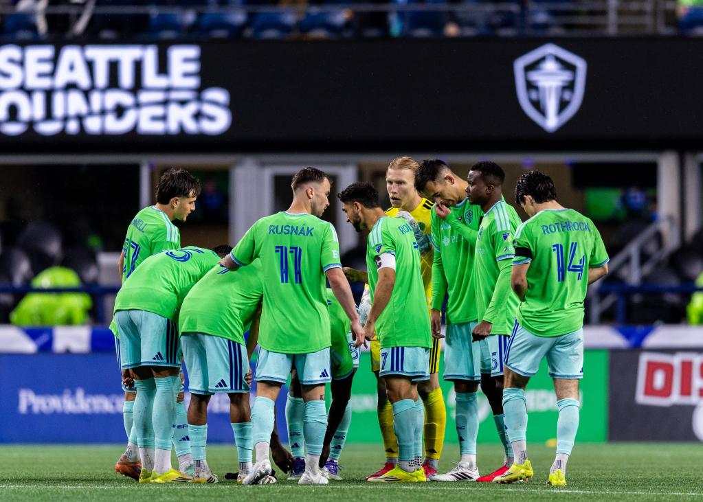 Seattle Sounders players huddle at midfield during a night game
