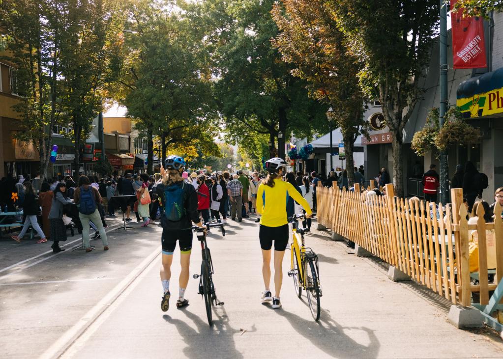 Two people walk their bicycles through a street festival in the U District neighborhood
