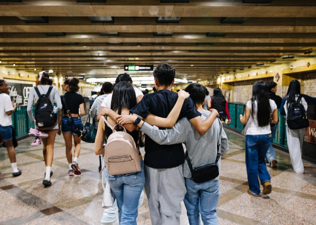 Three young people walk through Westlake Station wearing backpacks 