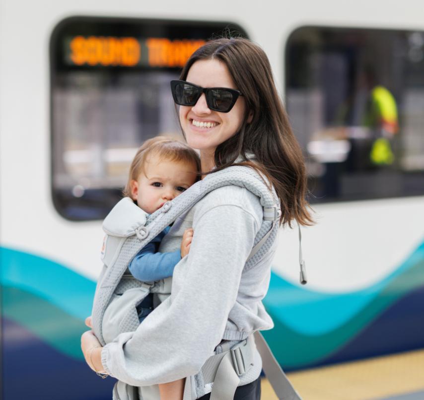 A woman smiling on a Link station platform holding a baby.