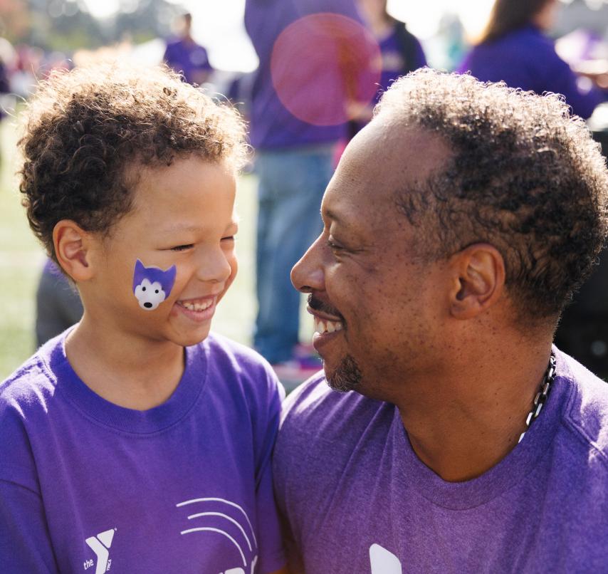 A child and an adult wearing purple YMCA shirts. The child has a UW husky facepainting.